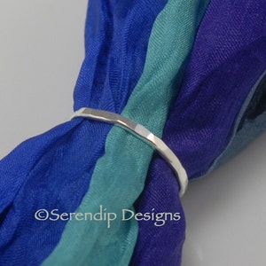 May include: A silver hammered ring, shown on a blue, teal, and purple scarf.  The ring is a simple band with a hammered texture.