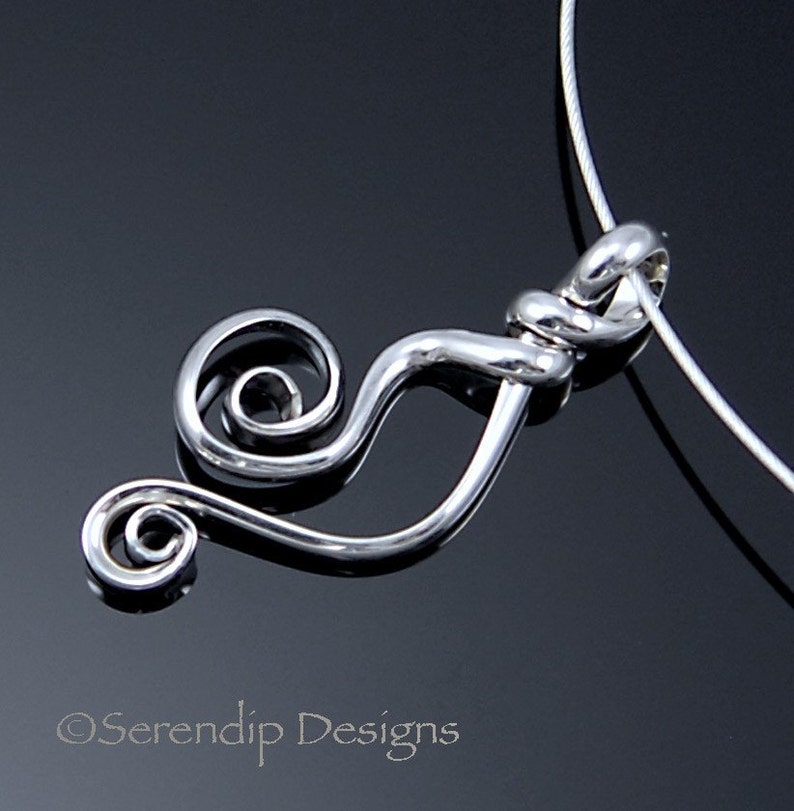 May include: A silver-colored pendant necklace with a swirling, abstract design. The pendant features a curved shape with a spiral at one end and is suspended from a thin, silver-colored chain. The background is a dark, reflective surface.