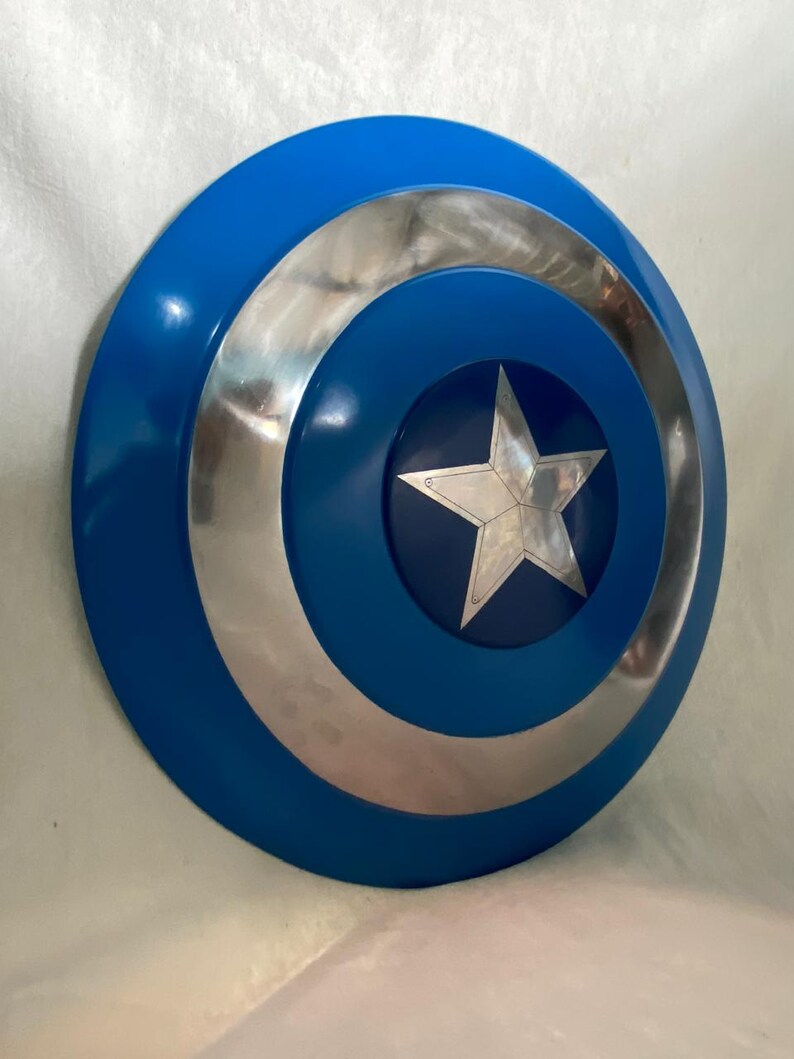 May include: A circular shield featuring a vibrant blue outer ring, a polished silver metallic middle ring, and a dark blue center circle. A five-pointed silver star is centered within the dark blue circle, displaying visible rivets at each point.
