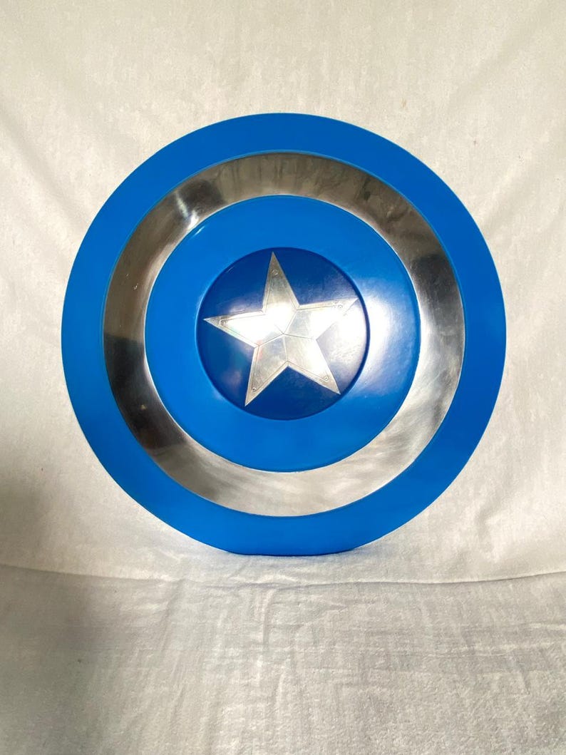 May include: A circular shield featuring a bright blue outer ring, a metallic silver middle ring, and a central blue circle containing a prominent five-pointed silver star. The design is symmetrical with a smooth, reflective finish throughout the surface.
