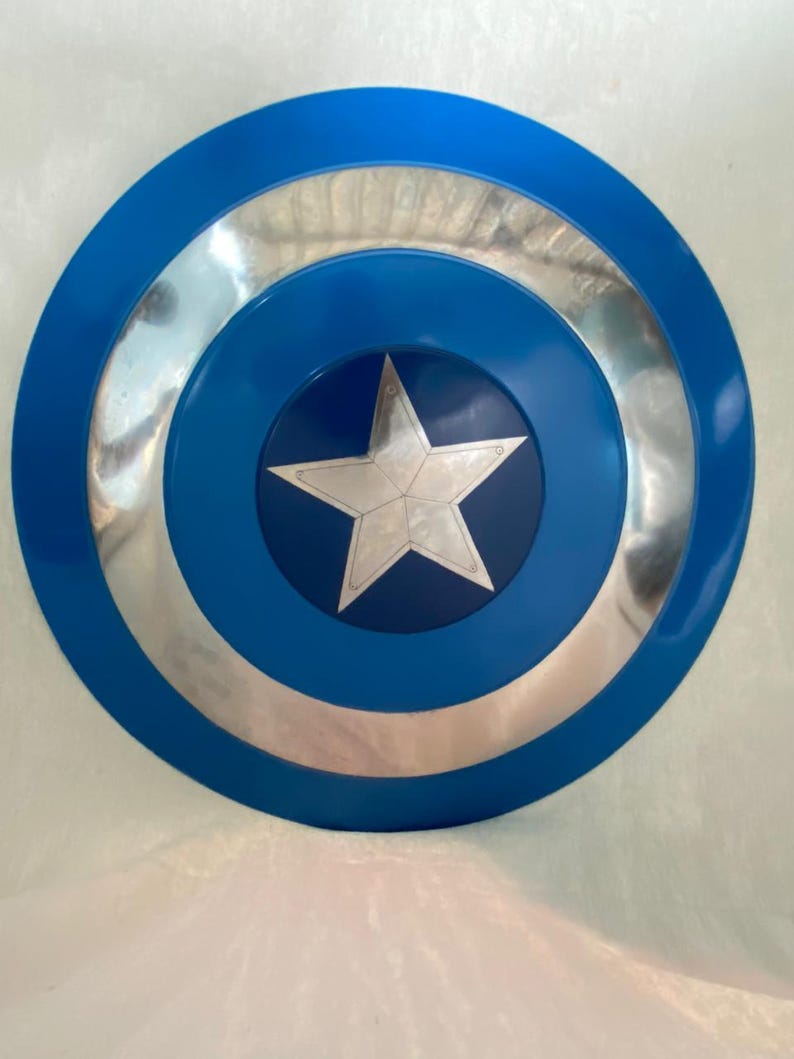 May include: A circular shield featuring a vibrant blue outer ring, a reflective silver middle ring, and a dark blue center circle. A prominent five-pointed silver star is centered within the dark blue circle, creating a bold, geometric design.