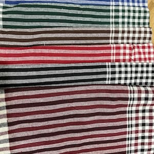 Puede incluir: Una pila de paños de tela coloridos, a rayas y a cuadros. Los paños presentan una variedad de colores, incluyendo azul, verde, marrón, rojo, negro y burdeos. La tela tiene un aspecto texturizado.