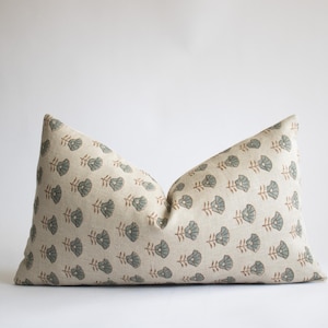 May include: A beige pillow with a floral pattern in shades of green and brown. The pillow is made of a soft, linen-like fabric.