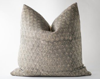 May include: A square throw pillow featuring a repeating pattern of small, dark gray leaf motifs printed on a muted, light gray fabric background. The pillow has a soft, plump appearance with a distinct crease at the top center.