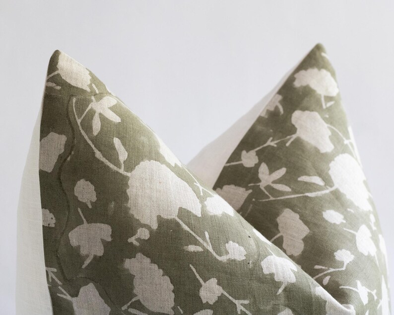 Puede incluir: Dos fundas de coj&iacute;n con estampado verde y blanco con un borde blanco. El estampado presenta un dise&ntilde;o floral con flores y hojas blancas sobre un fondo verde.