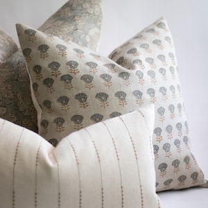 May include: A collection of three square and rectangular scatter cushions. One cushion features a repeating pattern of small blue-grey flowers with brown stems on a cream background. Another displays a dense floral print, while the third has vertical stripes.
