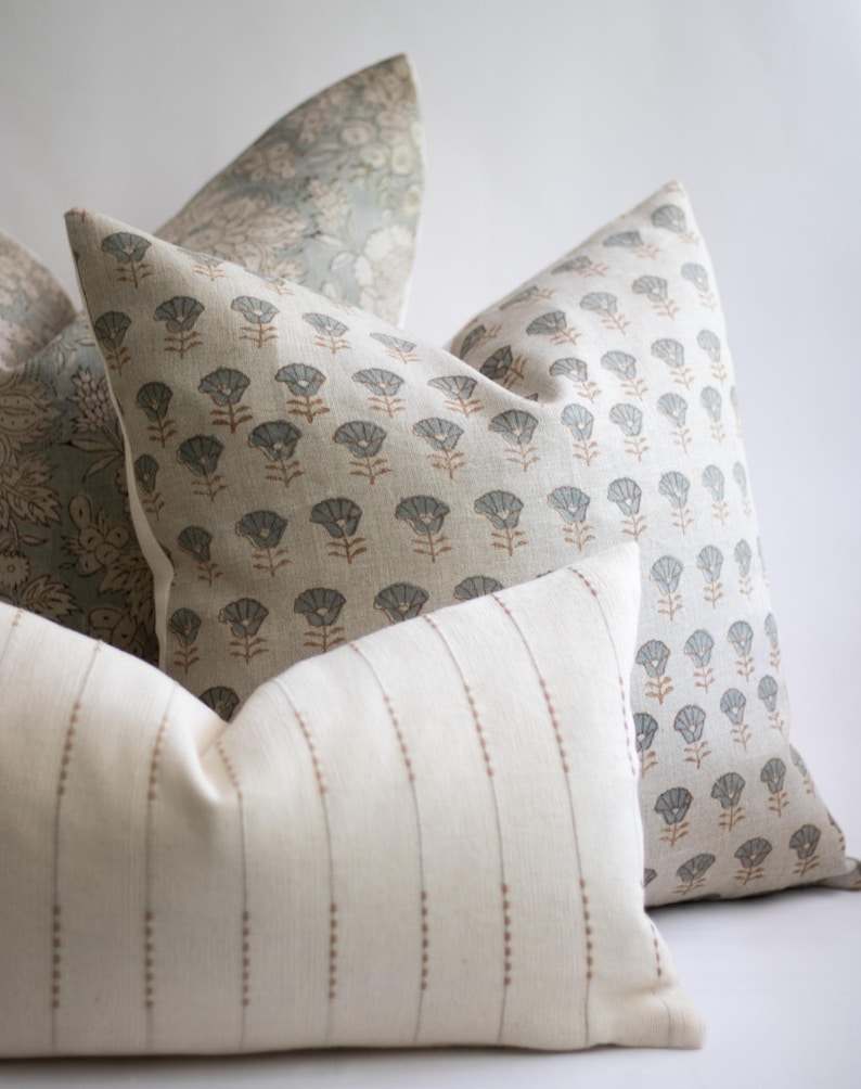May include: A collection of three square and rectangular scatter cushions. One cushion features a repeating pattern of small blue-grey flowers with brown stems on a cream background. Another displays a dense floral print, while the third has vertical stripes.