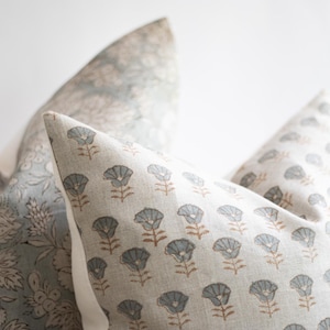 May include: A set of three decorative throw pillows featuring a light beige fabric base. One pillow displays a repeating pattern of small grey flowers with brown stems, while the others feature intricate, dense grey floral botanical prints.