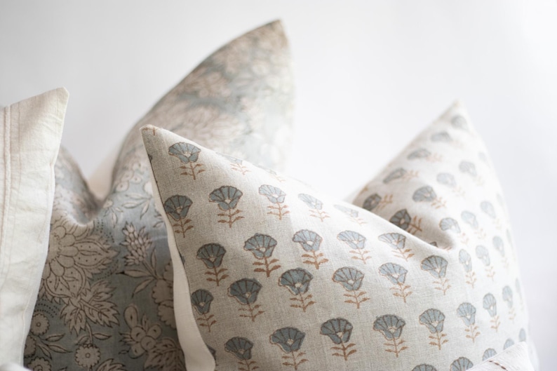 May include: A set of three decorative throw pillows featuring a light beige fabric base. One pillow displays a repeating pattern of small grey flowers with brown stems, while the others feature intricate, dense grey floral botanical prints.
