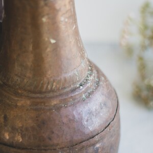 May include: A vintage copper pitcher with a worn, aged patina. The pitcher has a round body and a narrow neck with a handle.