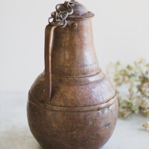 May include: A vintage copper pitcher with a hammered finish and a chain handle. The pitcher has a rounded body and a narrow neck.