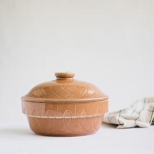 Op de afbeelding: Een bruine keramische ovenschaal met deksel. De schaal heeft een decoratief patroon van geweven lijnen en het deksel heeft een knop bovenop.