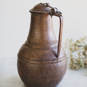 May include: A vintage copper pitcher with a hinged lid and a handle. The pitcher has a rounded body and a slightly flared spout. The copper has a patina of age and wear.