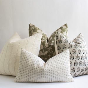 Puede incluir: Cinco almohadas decorativas con diferentes patrones. Dos almohadas son blancas con una textura sutil, una es blanca con rayas finas, una es verde con un patr&oacute;n floral y una es blanca con un patr&oacute;n floral negro.