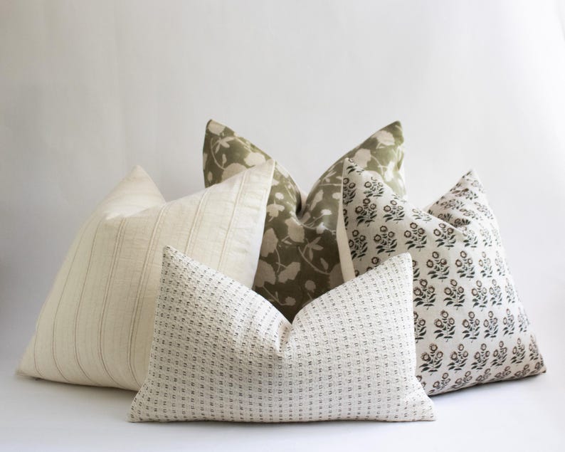 Puede incluir: Cinco almohadas decorativas con diferentes patrones. Dos almohadas son blancas con una textura sutil, una es blanca con rayas finas, una es verde con un patr&oacute;n floral y una es blanca con un patr&oacute;n floral negro.