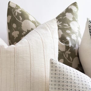 Puede incluir: Tres almohadas decorativas con diferentes patrones. La almohada del centro es blanca con rayas verticales. La almohada de la izquierda es verde con un patr&oacute;n floral. La almohada de la derecha es blanca con un peque&ntilde;o patr&oacute;n geom&eacute;trico negro.
