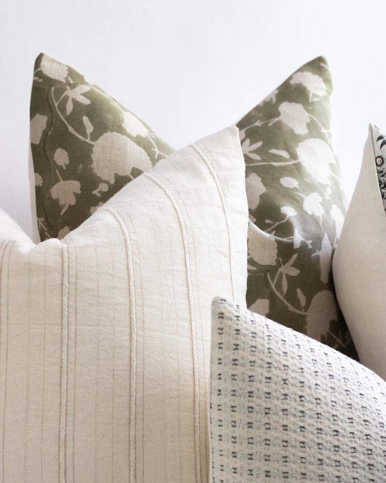 Puede incluir: Tres almohadas decorativas con diferentes patrones. La almohada del centro es blanca con rayas verticales. La almohada de la izquierda es verde con un patr&oacute;n floral. La almohada de la derecha es blanca con un peque&ntilde;o patr&oacute;n geom&eacute;trico negro.