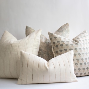May include: A collection of four decorative throw cushions in various shapes and sizes. One cushion features a cream fabric with vertical pinstripes, another has a rectangular shape with dotted lines, and two others display intricate floral patterns.