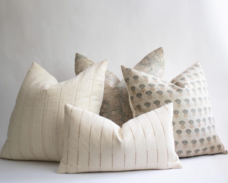 May include: A collection of four decorative throw cushions in various shapes and sizes. One cushion features a cream fabric with vertical pinstripes, another has a rectangular shape with dotted lines, and two others display intricate floral patterns.