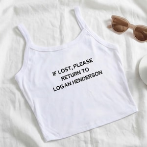 Könnte beinhalten: Weißes Tanktop mit dünnen Trägern. Der Text "IF LOST, PLEASE RETURN TO LOGAN HENDERSON" ist schwarz gedruckt. Eine Sonnenbrille und eine weiße Tasse befinden sich im Hintergrund.