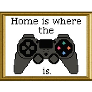 May include: A framed print with the text "Home is where the ___ is." with a black and gray video game controller in the center. The controller has colorful buttons.