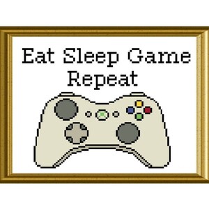 May include: A white video game controller with green, red, and yellow buttons. The text "Eat Sleep Game Repeat" is above the controller in a gold frame.