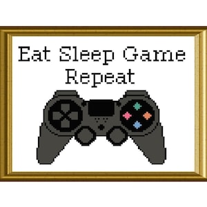May include: A framed cross-stitch design with the text "Eat Sleep Game Repeat" and a black video game controller.