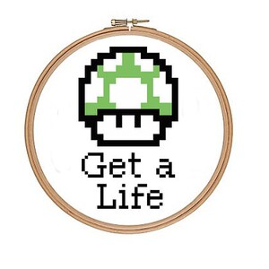 May include: A white embroidery hoop with a green and black pixelated mushroom graphic and the text "Get a Life".