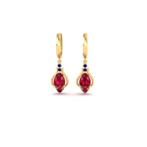 May include: A pair of gold-colored drop earrings. Each earring features a large, oval-shaped red gemstone, accented with smaller red and blue gemstones. The earrings have a decorative, openwork design.