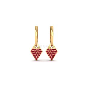 May include: A pair of gold-colored hoop earrings. Each earring features a diamond-shaped charm filled with small, round, red gemstones. The earrings are displayed against a white background, highlighting their design and color.