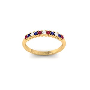 May include: A gold ring with a row of alternating red, white, and blue gemstones. The ring has a simple band and the gemstones are set close together. The text "Truegemsjewels" is on the ring.