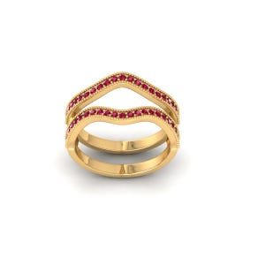 May include: A gold-colored ring with a double band design. The top band is a V-shape, and both bands are adorned with small, red gemstones. The ring has a textured, beaded edge.