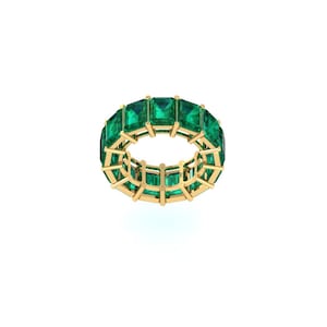 May include: A gold ring featuring a continuous band of emerald-cut green gemstones. The ring's setting is gold, and the gemstones are evenly spaced around the band. The ring is displayed against a white background.