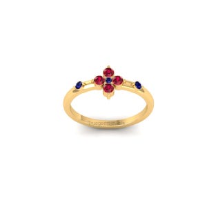 May include: A gold ring with a floral design, set with red and blue gemstones. The ring has a delicate band and a central cluster of red stones, with blue accents. The ring is displayed against a white background.
