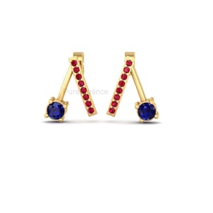 May include: A pair of gold earrings with a modern design. Each earring features a round, dark blue gemstone at the base and a line of small red gemstones. The earrings have a unique, angled shape.