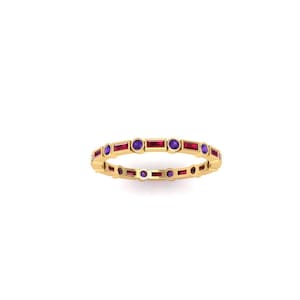 May include: A gold ring with alternating rectangular red and round purple gemstones. The ring is set against a white background, showcasing its intricate design and vibrant colors. The ring is a piece of jewelry.