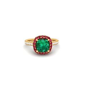 May include: A gold ring featuring a large, square-cut emerald center stone surrounded by a halo of small red gemstones. The ring's band is also adorned with small, clear gemstones. The ring is set against a white background.