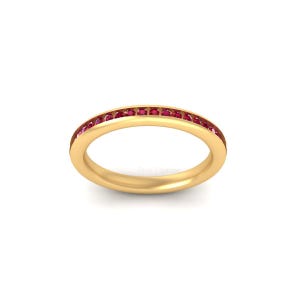 May include: A gold band ring with a continuous row of small, red gemstones set around the top. The ring is displayed on a white background, showcasing its polished finish and the vibrant color of the gemstones.
