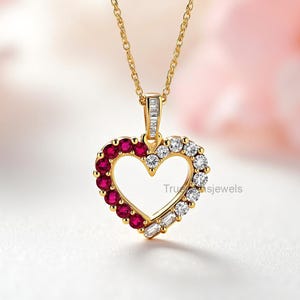 May include: A gold-colored heart pendant necklace. The heart is outlined with red and white gemstones. The necklace has a delicate gold chain. The pendant has the text "Tru...sjewels".
