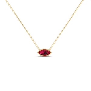 May include: A gold-colored necklace with a marquise-shaped, deep red gemstone pendant. The pendant is framed by a beaded border. The chain is delicate and has a link design. The necklace is displayed against a white background.