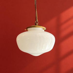 May include: A pendant light fixture featuring a smooth, opaque white glass globe shade. The shade is attached to a brass-toned metal cap and hardware, which connects to a matching brass-toned metal chain for suspension from a ceiling.
