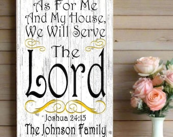 May include: A white wooden sign with the text "As For Me And My House, We Will Serve The Lord" in black script. The sign also includes the text "Joshua 24:15" and "The Johnson Family". A vase of pink roses sits to the right.