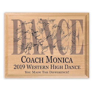 May include: A wooden plaque with the word "DANCE" in large letters, surrounded by many signatures. The plaque also reads "Coach Monica 2019 Western High Dance You Made The Difference!"