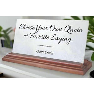 May include: White marble plaque with a wooden base. The plaque has the text "Choose Your Own Quote or Favorite Saying." and "Quote Credit" printed on it.