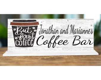 May include: White wooden sign with black text that reads "But first coffee" with a coffee cup graphic. The sign also says "Jonathan and Marianne's Coffee Bar".