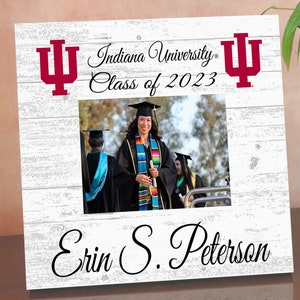 May include: White wooden picture frame with a red Indiana University logo and the text "Indiana University Class of 2023". The frame has a photo of a person in a graduation cap and gown. The name "Erin S. Peterson" is written at the bottom of the frame.