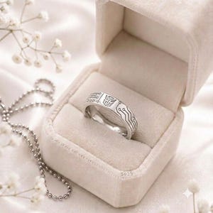 Könnte beinhalten: Ein silberfarbener Ring mit eingraviertem Autobot-Symbol und Leiterplattenmuster, gekennzeichnet mit S925, in einer beigen Samt-Ringbox. Der Ring hat eine polierte Oberfläche mit detaillierten, schwarz ausgefüllten Linien für Schaltkreise.