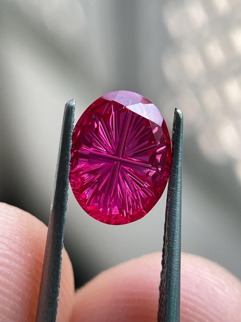Peut inclure: Une pierre pr&eacute;cieuse ovale d'un rouge magenta vibrant, pr&eacute;sentant un motif de taille complexe en forme d'&eacute;toile sur sa surface. La pierre affiche une saturation profonde et une grande clart&eacute;, la lumi&egrave;re se refl&eacute;tant sur les facettes.
