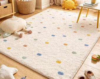 Op de afbeelding: Een crèmekleurig, rechthoekig vloerkleed met een speels stippenpatroon in diverse kleuren. Het vloerkleed is gemaakt van een zacht, pluche materiaal en is geschikt voor een kinderkamer of speelkamer. Het vloerkleed ligt op een houten vloer.