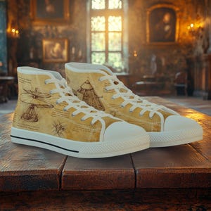 May include: A pair of high-top canvas sneakers with a tan background and white laces. The sneakers feature sketches of Leonardo da Vinci's inventions. The soles are white with a black stripe, and the shoes are displayed on a wooden surface.